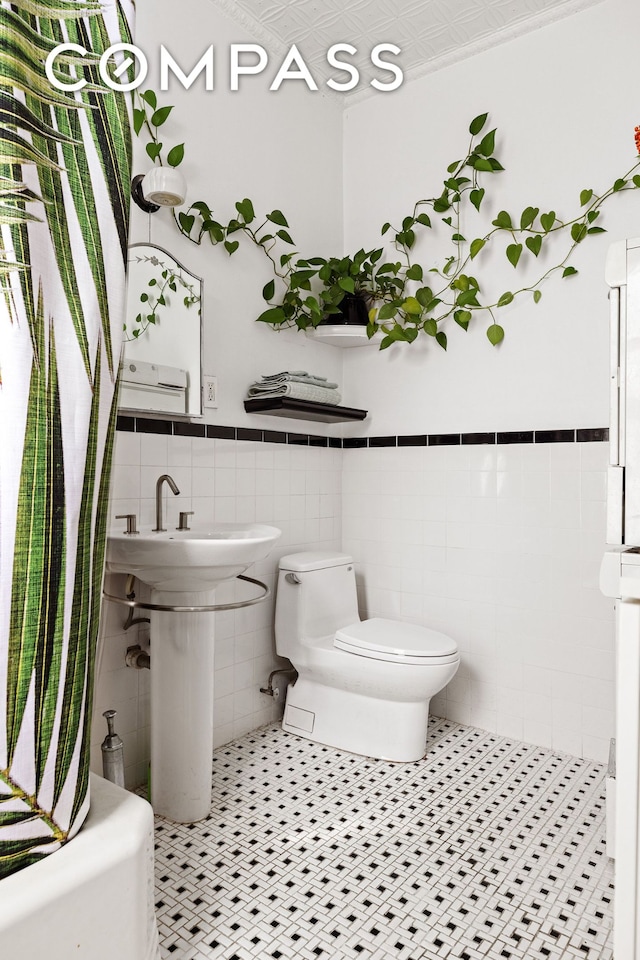 full bath with tile patterned flooring, wainscoting, toilet, and tile walls