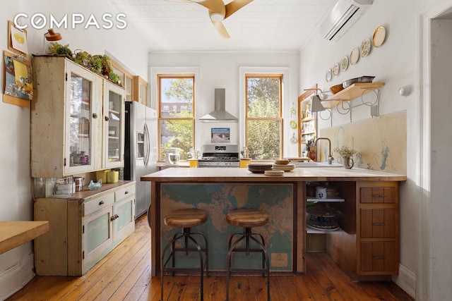 bar with hardwood / wood-style floors, appliances with stainless steel finishes, wall chimney exhaust hood, and a wall unit AC