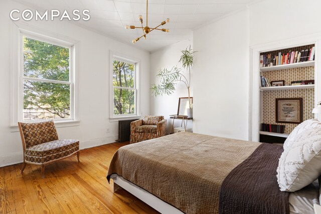 bedroom featuring an inviting chandelier, radiator heating unit, wood finished floors, and baseboards