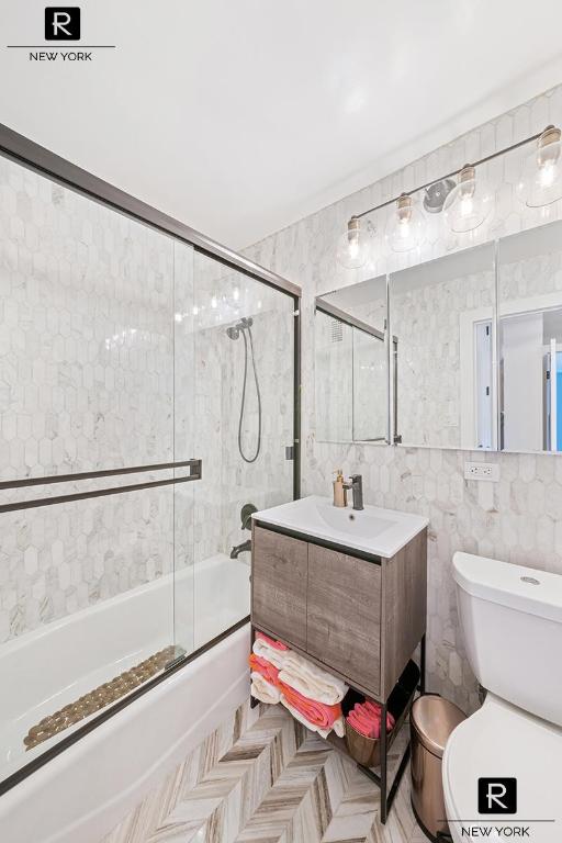 full bathroom with tile walls, combined bath / shower with glass door, vanity, and toilet