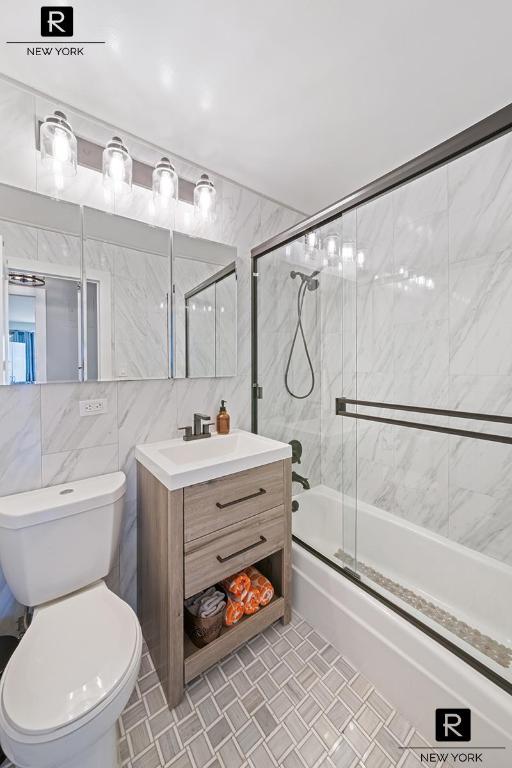 bathroom featuring tile walls, backsplash, toilet, combined bath / shower with glass door, and vanity