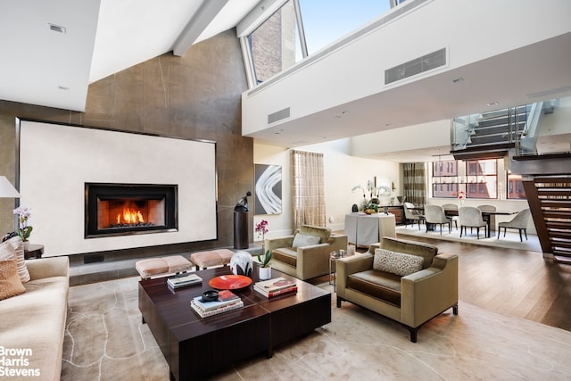 living room featuring visible vents, a high ceiling, a warm lit fireplace, and wood finished floors