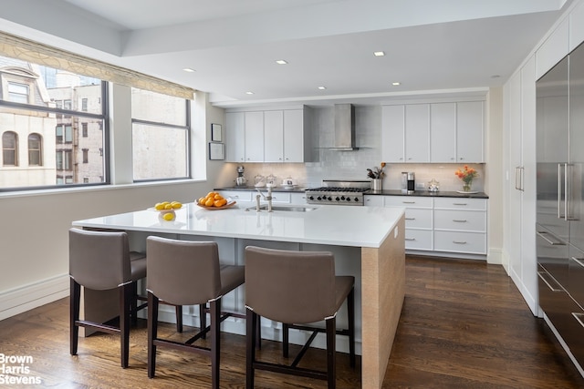 kitchen featuring stainless steel built in refrigerator, a breakfast bar area, dark wood-type flooring, a center island with sink, and wall chimney exhaust hood