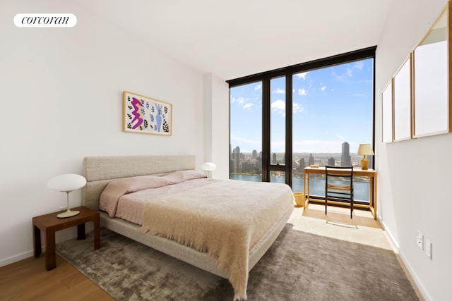 bedroom with wood-type flooring, a water view, and a wall of windows