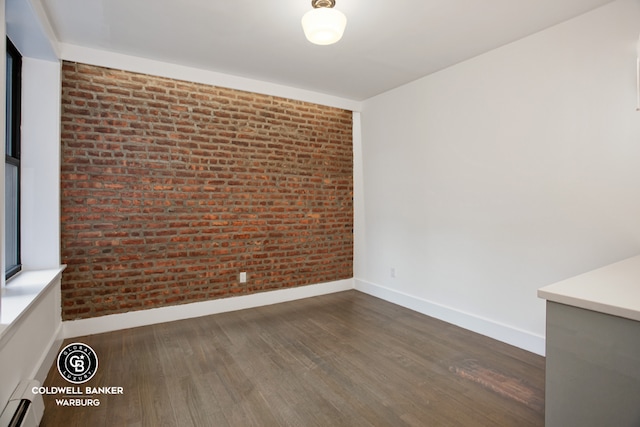 unfurnished room featuring baseboard heating, dark hardwood / wood-style flooring, and brick wall