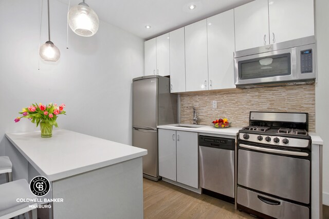 kitchen with tasteful backsplash, pendant lighting, kitchen peninsula, white cabinetry, and appliances with stainless steel finishes