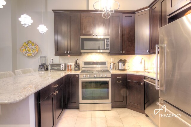 kitchen featuring light stone counters, stainless steel appliances, backsplash, a sink, and a peninsula