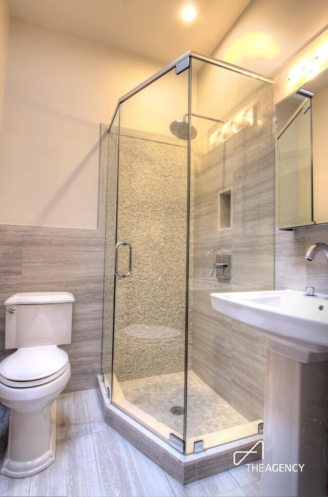 bathroom with a stall shower, tile walls, wainscoting, toilet, and a sink