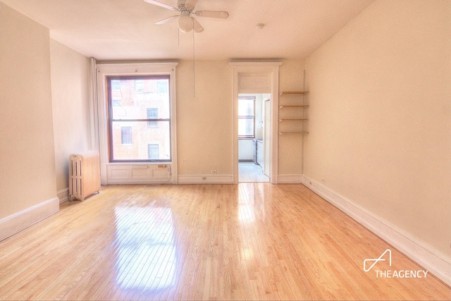 spare room featuring a ceiling fan, baseboards, light wood-style floors, and radiator heating unit