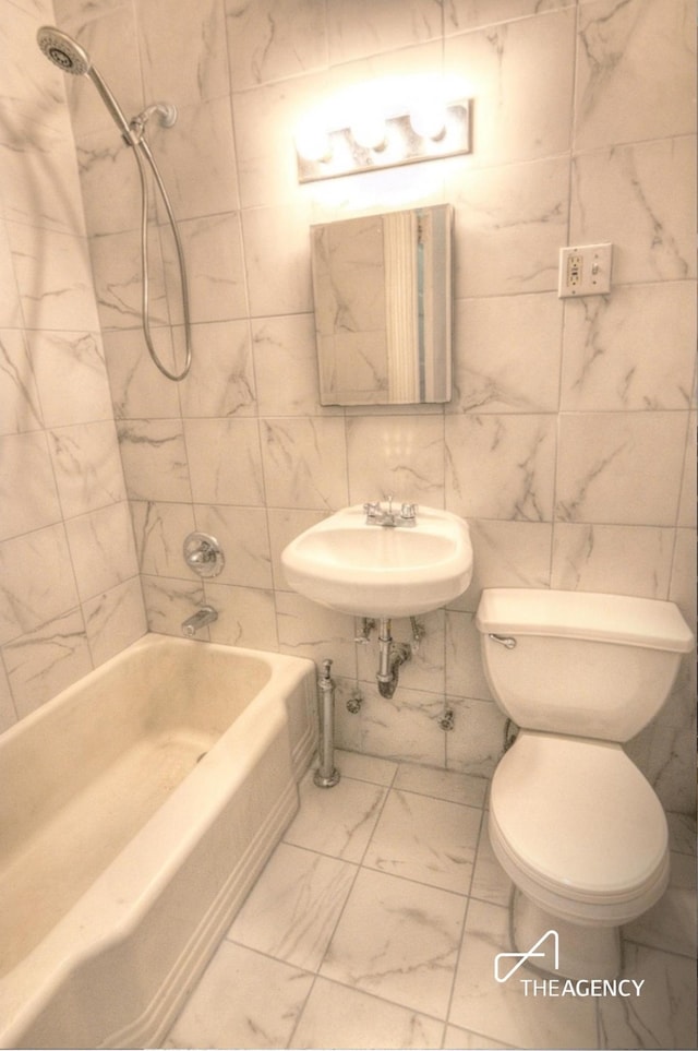 bathroom featuring toilet, marble finish floor, shower / bathtub combination, and a sink