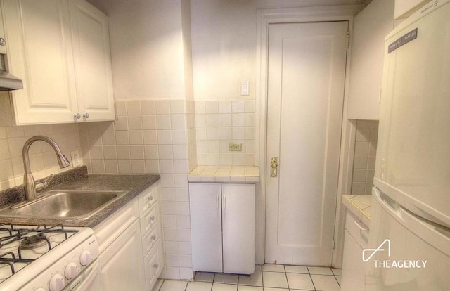 kitchen with light tile patterned floors, a sink, tile walls, white cabinetry, and freestanding refrigerator