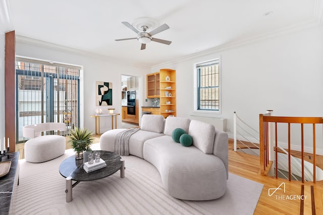 living room featuring light wood-style floors, baseboards, a ceiling fan, and crown molding