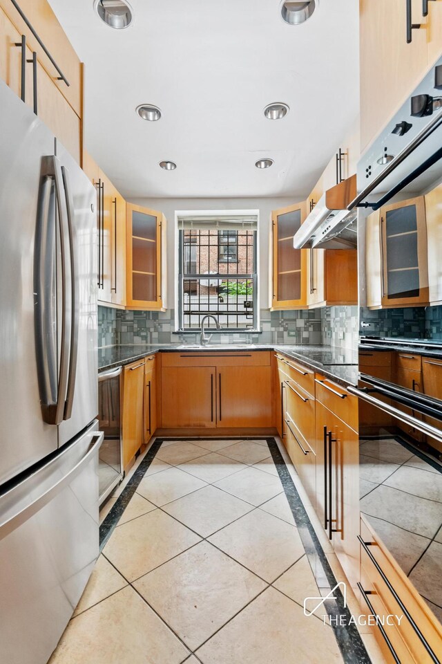 kitchen with light tile patterned floors, glass insert cabinets, a sink, and freestanding refrigerator