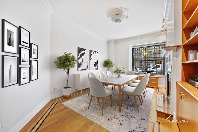 dining space with crown molding, rail lighting, baseboards, and light wood-type flooring