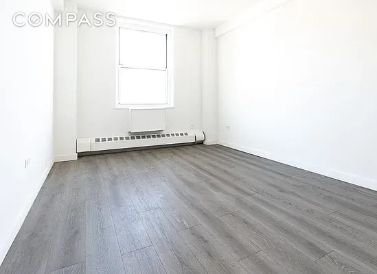 empty room featuring baseboards, wood finished floors, and a baseboard radiator