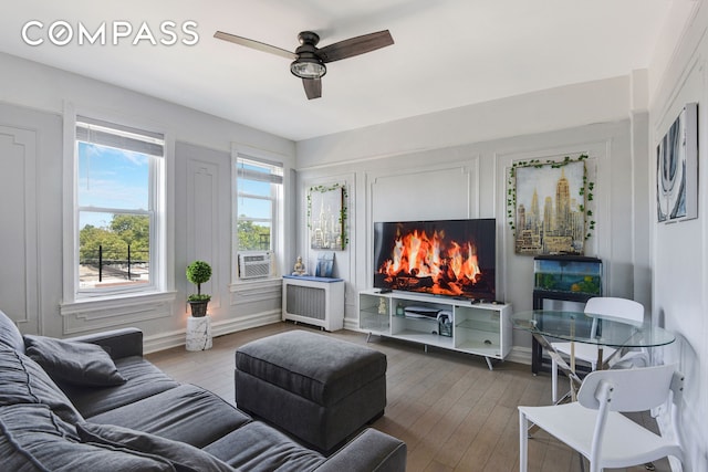 living area with cooling unit, a fireplace, wood finished floors, a ceiling fan, and radiator