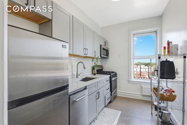 kitchen with stainless steel appliances, light countertops, a sink, and gray cabinetry