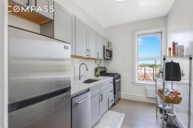 kitchen featuring baseboards, light wood finished floors, a sink, stainless steel appliances, and backsplash