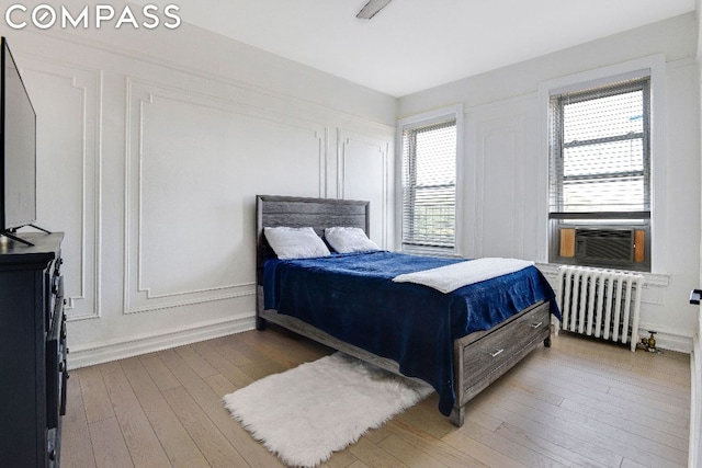 bedroom with cooling unit, radiator heating unit, and hardwood / wood-style floors