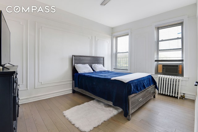 bedroom with a decorative wall, cooling unit, radiator heating unit, and wood finished floors