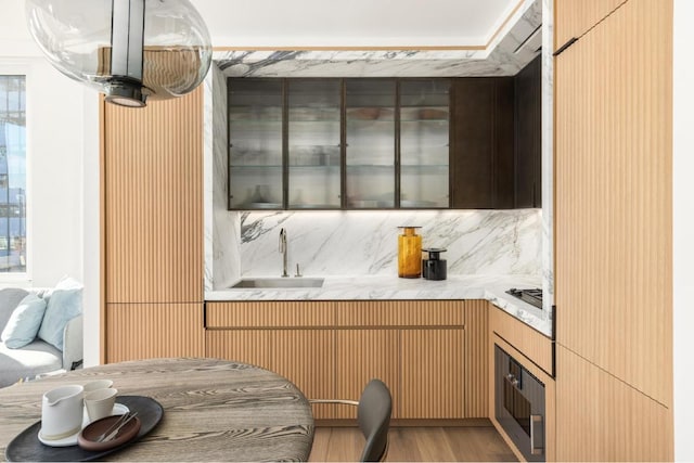 kitchen with sink, tasteful backsplash, light brown cabinets, wall oven, and light hardwood / wood-style floors