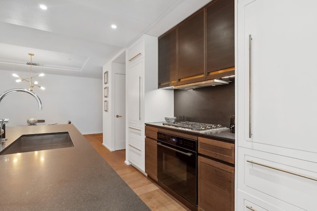 kitchen featuring stainless steel gas cooktop, sink, dark brown cabinets, black oven, and light hardwood / wood-style floors