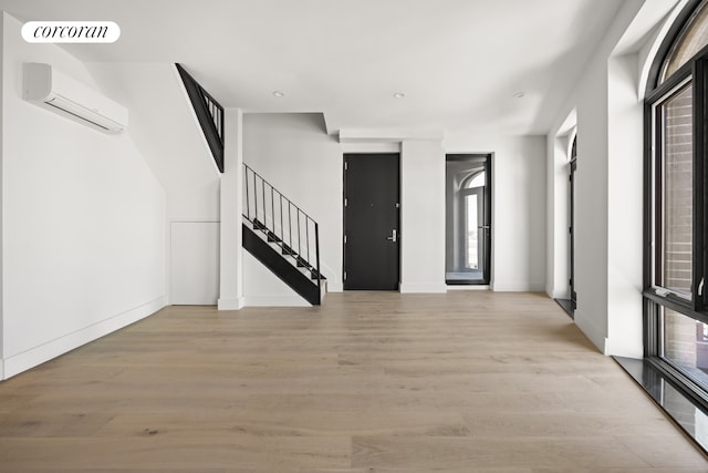 foyer with an AC wall unit, stairway, visible vents, and light wood finished floors