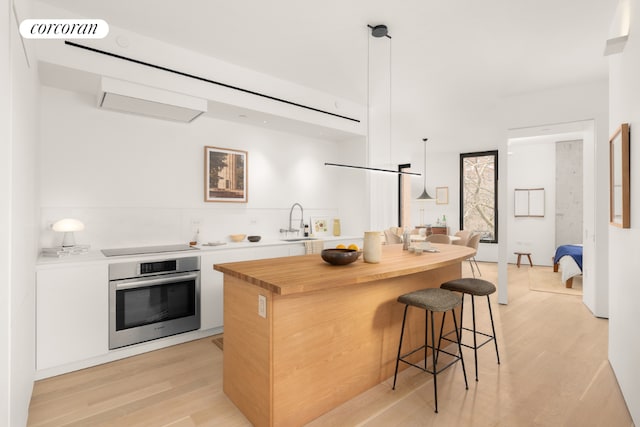 kitchen with light hardwood / wood-style flooring, sink, white cabinetry, decorative light fixtures, and stainless steel oven