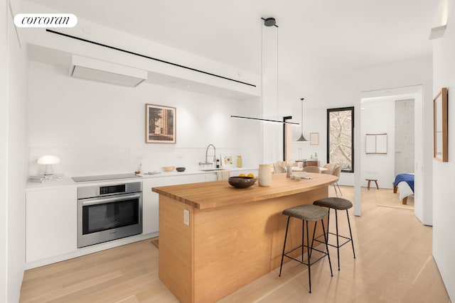 kitchen featuring oven, a breakfast bar, butcher block countertops, a sink, and light wood-type flooring