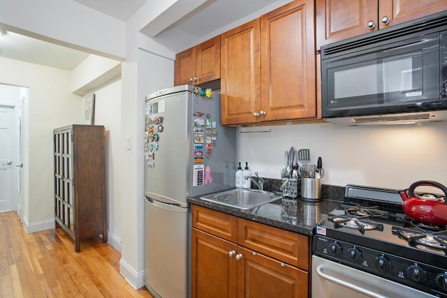 kitchen with stainless steel appliances, sink, light hardwood / wood-style floors, and dark stone counters