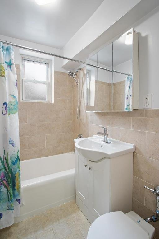 full bathroom with tile walls, shower / bath combination with curtain, vanity, and toilet