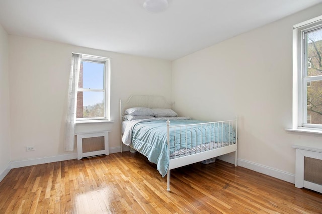 bedroom with hardwood / wood-style flooring, radiator, and multiple windows