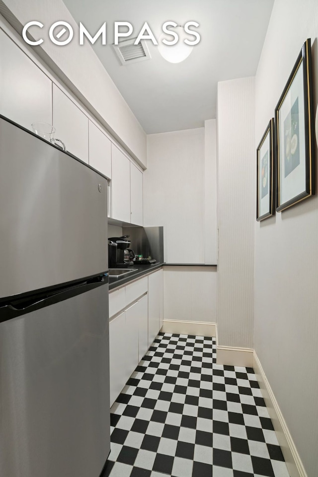 kitchen featuring dark countertops, freestanding refrigerator, white cabinetry, and dark floors