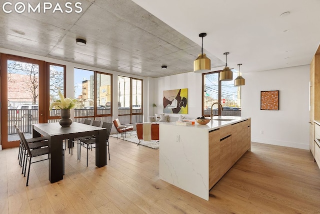 kitchen with decorative light fixtures, sink, light hardwood / wood-style floors, and an island with sink