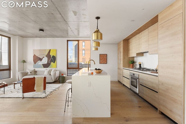 kitchen featuring decorative light fixtures, appliances with stainless steel finishes, a kitchen island with sink, and light wood-type flooring