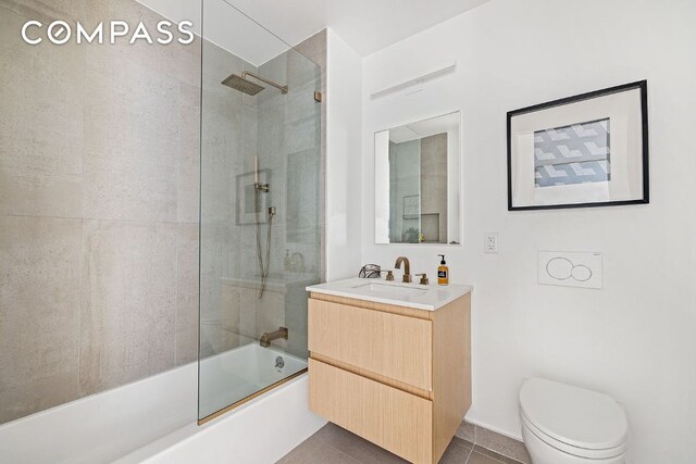 bathroom featuring toilet, vanity, tile walls, tile patterned flooring, and a tile shower