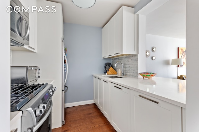 kitchen featuring dark wood-type flooring, a sink, backsplash, white cabinetry, and stainless steel appliances