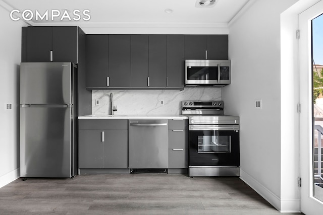 kitchen with light wood finished floors, stainless steel appliances, light countertops, backsplash, and a sink