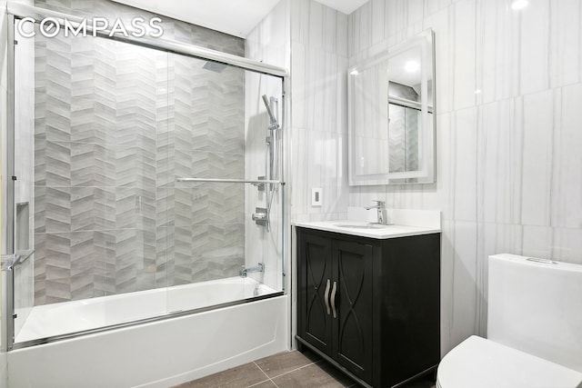 full bathroom featuring shower / bath combination with glass door, tile walls, toilet, vanity, and tile patterned floors