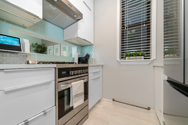 kitchen with extractor fan, backsplash, stainless steel range with gas stovetop, and white cabinetry