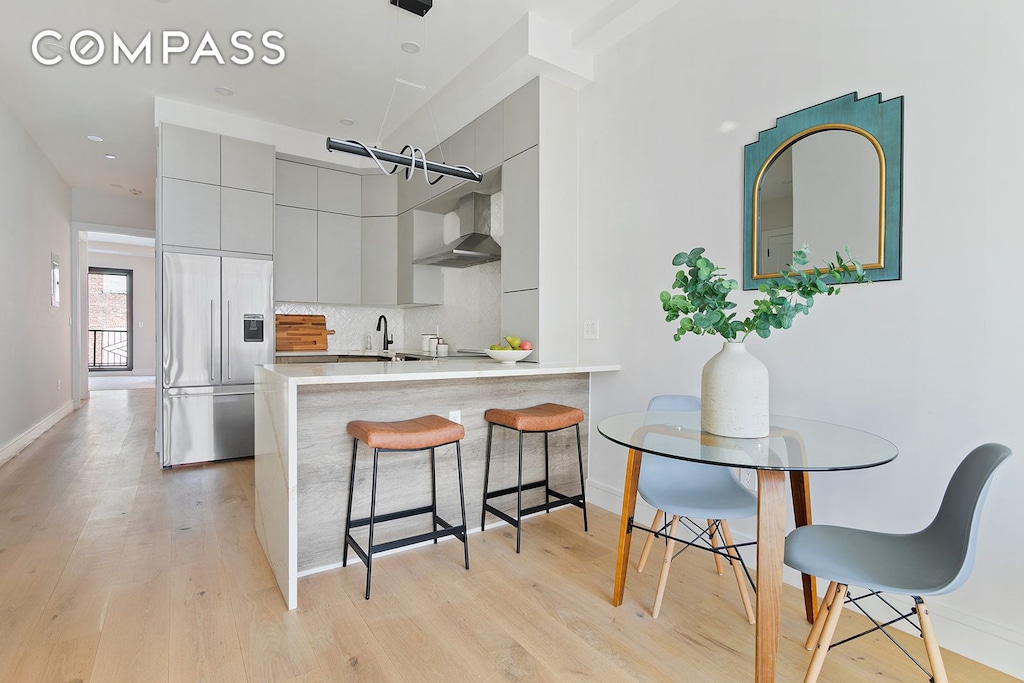 kitchen with a breakfast bar, modern cabinets, built in fridge, wall chimney range hood, and decorative backsplash