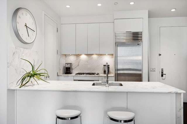 kitchen featuring stainless steel appliances, a sink, white cabinets, modern cabinets, and a kitchen bar