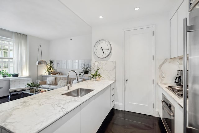 kitchen with white cabinets, light stone counters, stainless steel appliances, and a sink