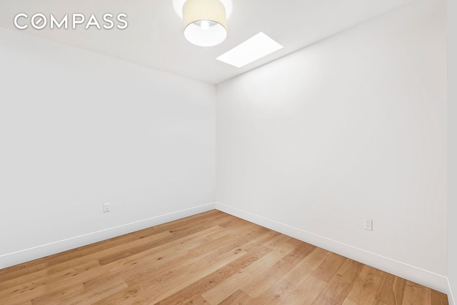 unfurnished room featuring a skylight, baseboards, and light wood-type flooring