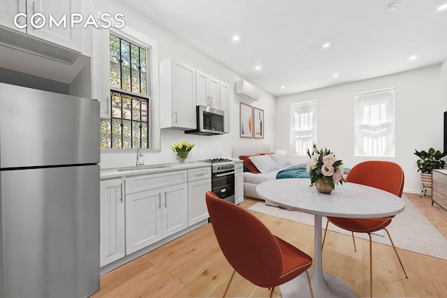 kitchen with light wood finished floors, a sink, stainless steel appliances, an AC wall unit, and white cabinetry