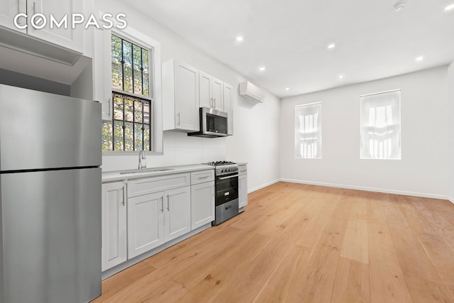 kitchen featuring tasteful backsplash, a wall mounted air conditioner, appliances with stainless steel finishes, white cabinetry, and a sink