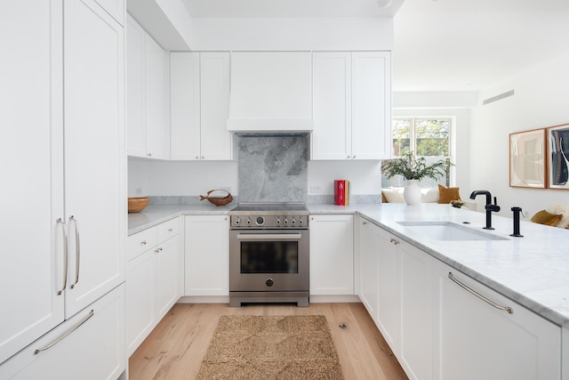 kitchen featuring light wood-type flooring, light stone counters, stainless steel range with electric stovetop, white cabinets, and a sink