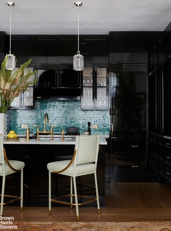 kitchen featuring sink, backsplash, a kitchen breakfast bar, hanging light fixtures, and hardwood / wood-style flooring