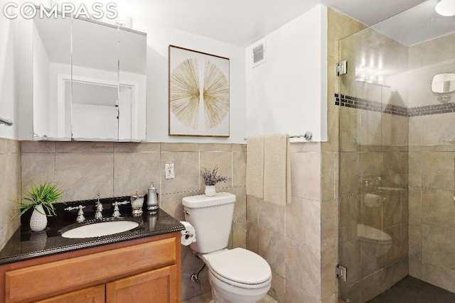 bathroom with vanity, toilet, a shower with shower door, and tile walls