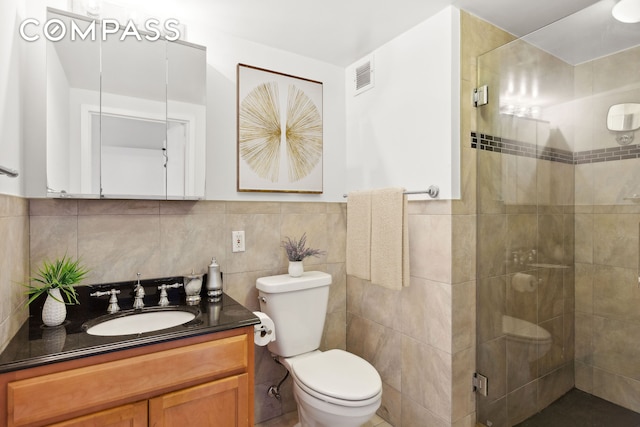 full bath with visible vents, toilet, vanity, a shower stall, and tile walls